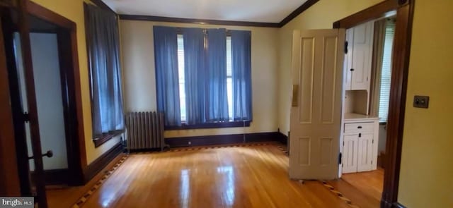 empty room featuring radiator, light hardwood / wood-style flooring, and ornamental molding