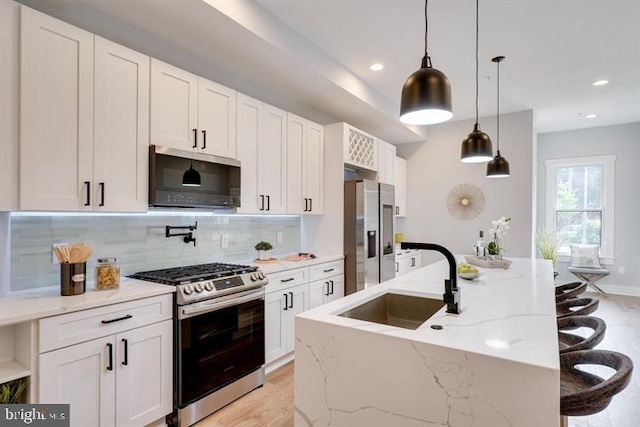 kitchen featuring stainless steel appliances, light stone countertops, white cabinets, and sink