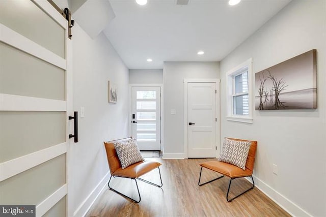 sitting room featuring light wood-type flooring, a barn door, and a healthy amount of sunlight