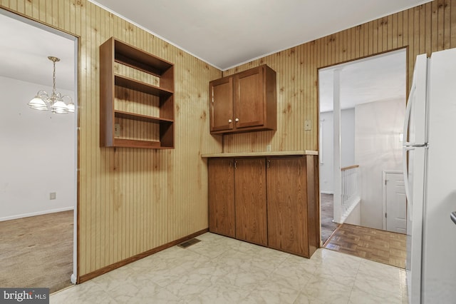 kitchen featuring a notable chandelier, wood walls, white refrigerator, and hanging light fixtures