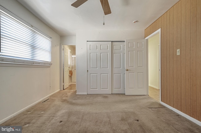 unfurnished bedroom with a closet, wood walls, light colored carpet, and ceiling fan