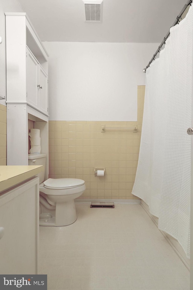 bathroom with toilet, walk in shower, vanity, and tile walls