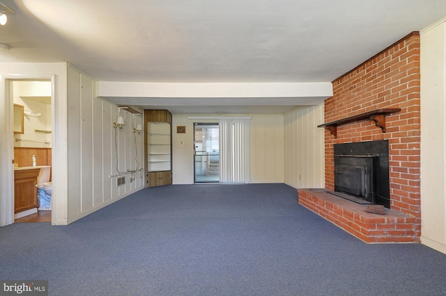 unfurnished living room featuring wood walls, carpet flooring, beamed ceiling, and a brick fireplace