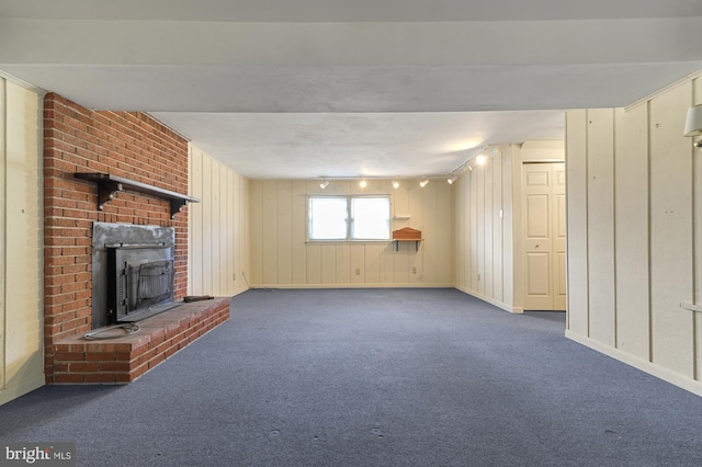 unfurnished living room with dark carpet, track lighting, and a brick fireplace