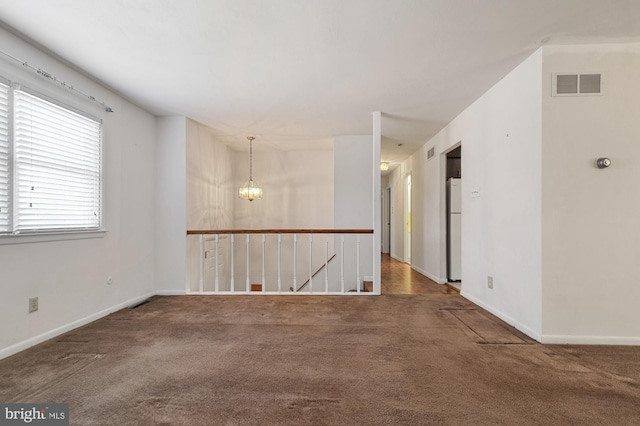 carpeted spare room featuring an inviting chandelier