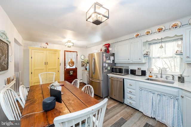 kitchen featuring tasteful backsplash, stainless steel appliances, hanging light fixtures, sink, and light hardwood / wood-style flooring