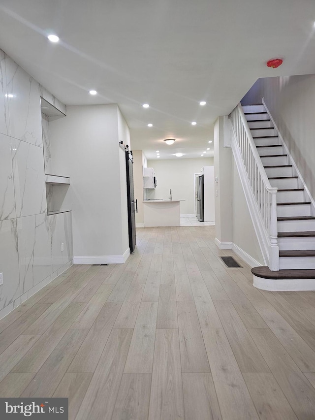 basement featuring a barn door, stainless steel refrigerator, and light hardwood / wood-style flooring