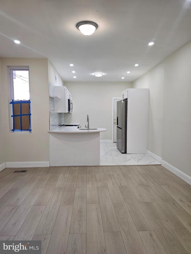 kitchen with sink, light hardwood / wood-style flooring, kitchen peninsula, white cabinets, and appliances with stainless steel finishes