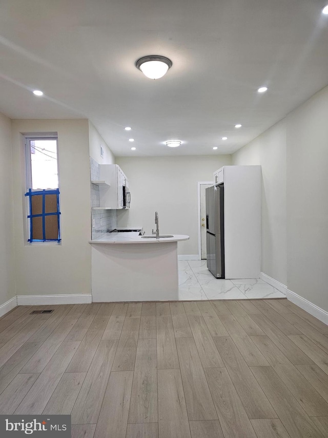 kitchen featuring sink, kitchen peninsula, stainless steel fridge, light hardwood / wood-style floors, and white cabinetry