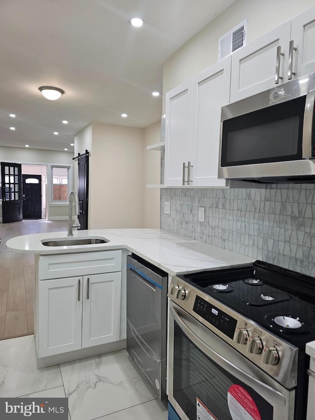 kitchen with kitchen peninsula, a barn door, stainless steel appliances, and white cabinetry