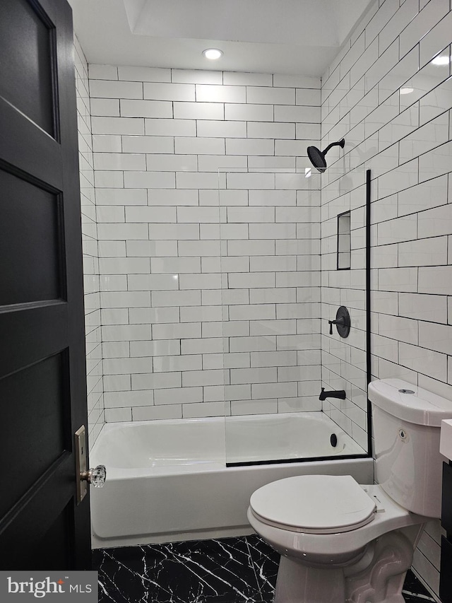 bathroom featuring tiled shower / bath combo, toilet, and tile walls