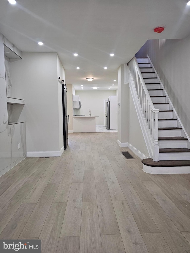 unfurnished living room with a barn door and light hardwood / wood-style flooring