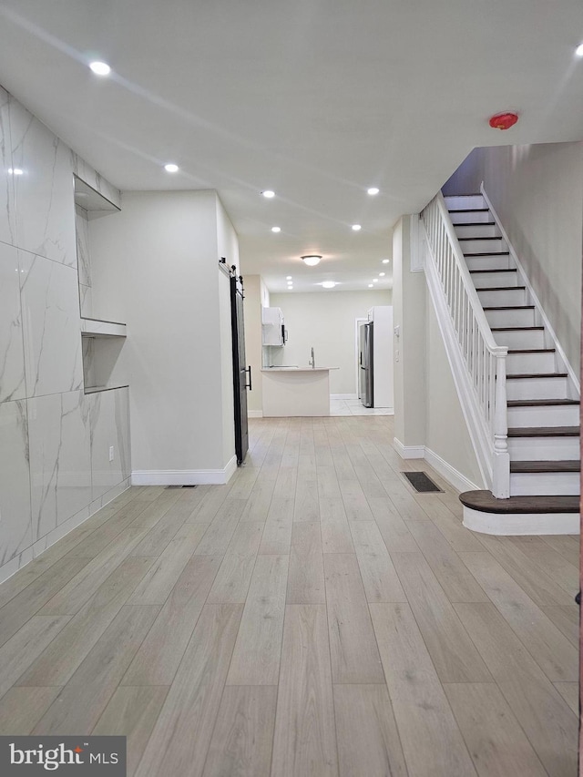 basement featuring stainless steel fridge, a barn door, and light hardwood / wood-style floors