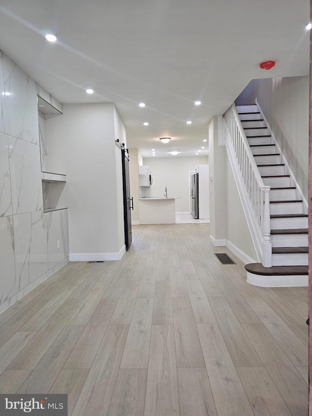 basement with stainless steel fridge, a barn door, and light hardwood / wood-style flooring