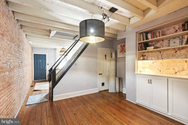 unfurnished living room with beamed ceiling, brick wall, and dark wood-type flooring