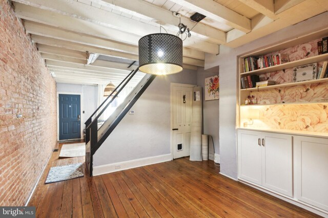 interior space with beam ceiling, brick wall, hardwood / wood-style floors, and baseboards