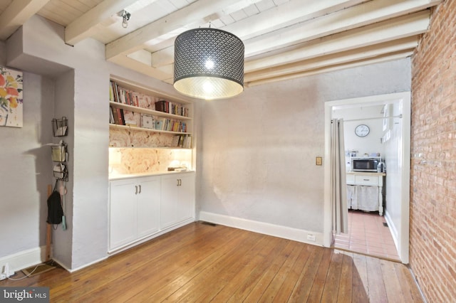 unfurnished dining area featuring light wood-type flooring, built in features, beamed ceiling, and baseboards