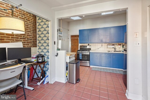 kitchen with brick wall, stainless steel gas stove, blue cabinets, and tile patterned flooring