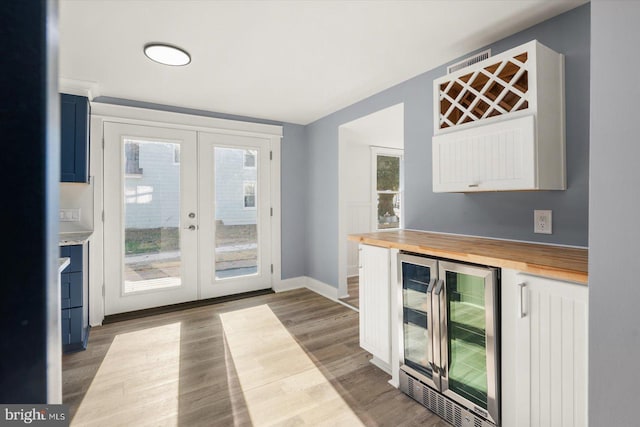 bar with wooden counters, beverage cooler, french doors, and light hardwood / wood-style flooring