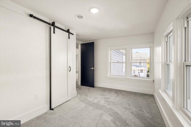 unfurnished bedroom featuring a barn door and light colored carpet