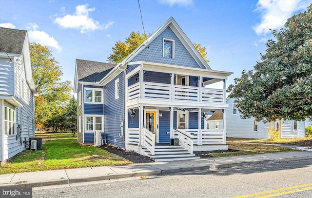 view of front of home featuring covered porch, a balcony, cooling unit, and a front yard