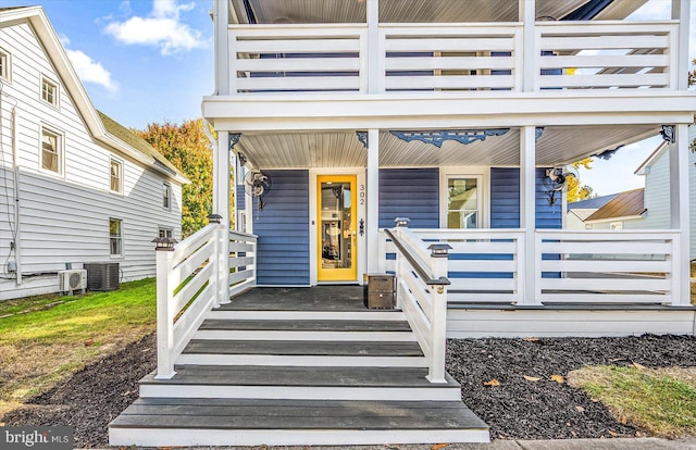 view of exterior entry with covered porch, a balcony, and central AC