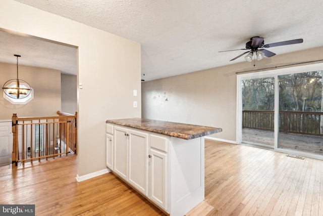 kitchen with kitchen peninsula, pendant lighting, light hardwood / wood-style floors, white cabinets, and ceiling fan with notable chandelier