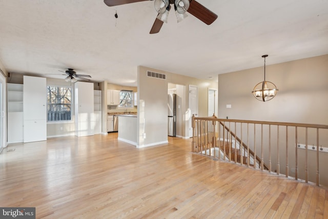 unfurnished living room featuring ceiling fan with notable chandelier and light wood-type flooring