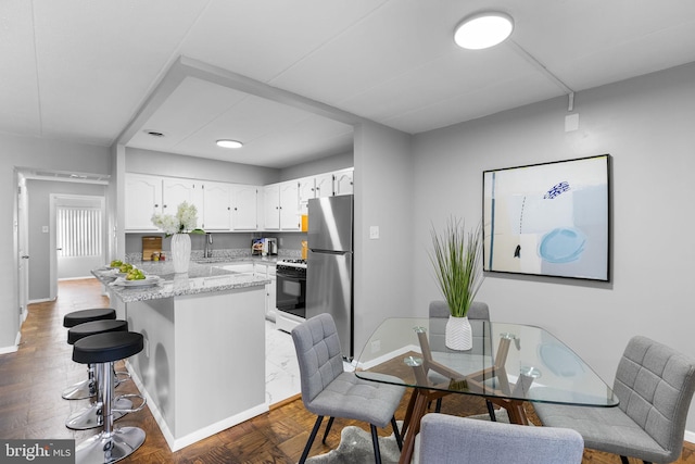 kitchen featuring black stove, a kitchen breakfast bar, white cabinets, light stone counters, and stainless steel refrigerator