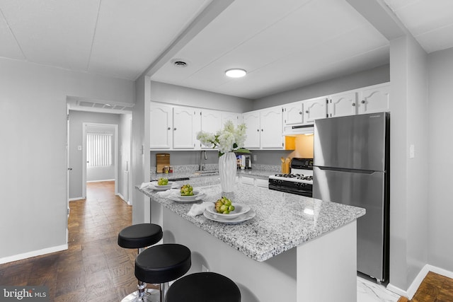 kitchen featuring stainless steel fridge, white cabinetry, a breakfast bar, and gas range gas stove