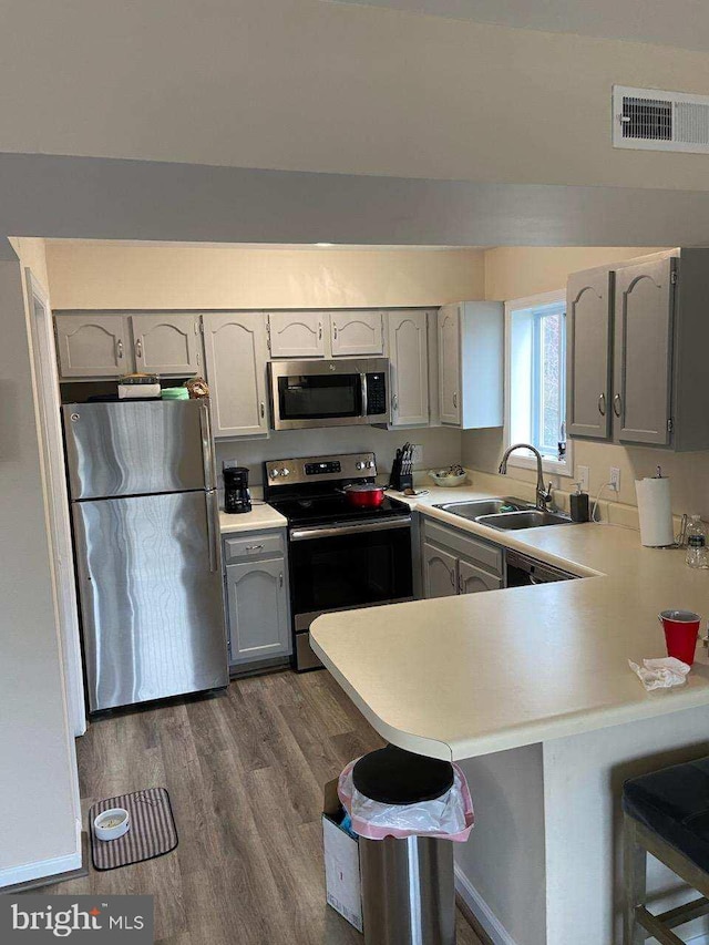 kitchen with a breakfast bar, sink, gray cabinets, kitchen peninsula, and stainless steel appliances