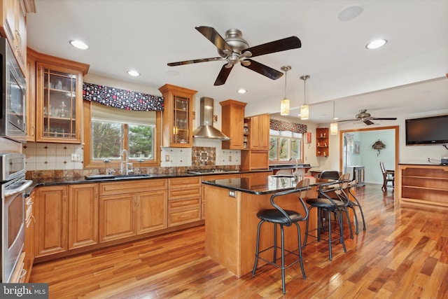 kitchen with wall chimney exhaust hood, a healthy amount of sunlight, light hardwood / wood-style flooring, and a kitchen island