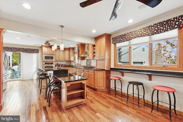 kitchen with light hardwood / wood-style floors, appliances with stainless steel finishes, a breakfast bar area, hanging light fixtures, and decorative backsplash