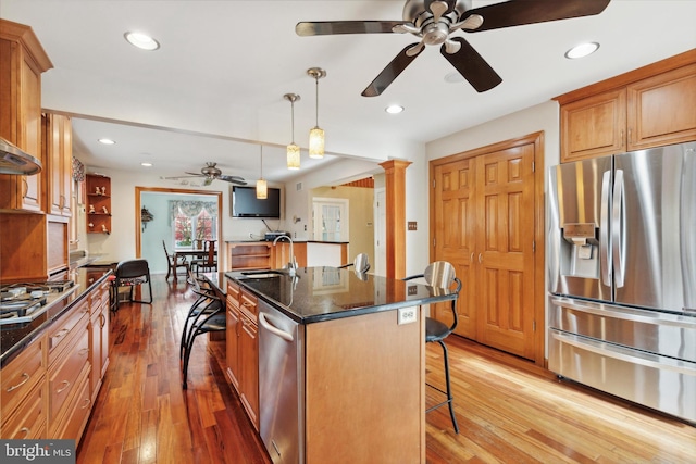 kitchen featuring stainless steel appliances, a kitchen bar, hanging light fixtures, hardwood / wood-style flooring, and an island with sink