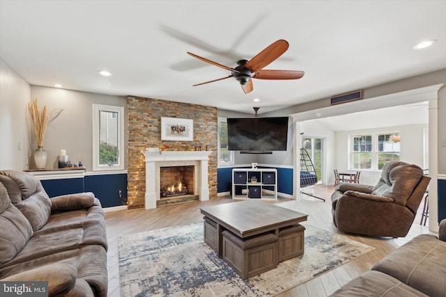 living room with a stone fireplace, ceiling fan, and light hardwood / wood-style flooring