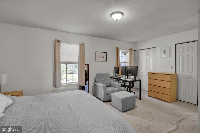 bedroom featuring multiple closets, light colored carpet, and a textured ceiling