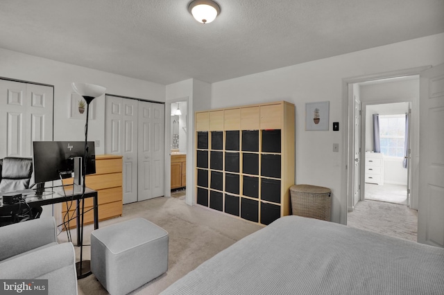 bedroom with light colored carpet, two closets, a textured ceiling, and ensuite bathroom