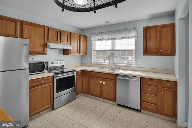 kitchen with under cabinet range hood, brown cabinetry, appliances with stainless steel finishes, and a sink