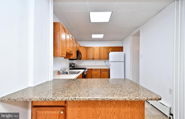 kitchen featuring baseboard heating, stainless steel gas stove, white refrigerator, a drop ceiling, and kitchen peninsula