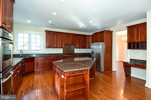 kitchen with appliances with stainless steel finishes, hardwood / wood-style flooring, dark stone counters, sink, and a center island