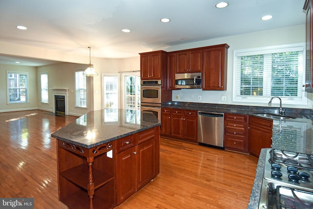 kitchen with appliances with stainless steel finishes, sink, a kitchen island, light hardwood / wood-style floors, and dark stone countertops