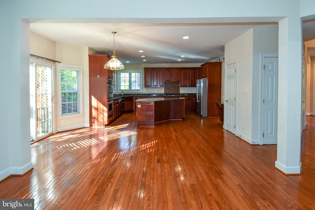 kitchen with backsplash, dark hardwood / wood-style flooring, stainless steel appliances, decorative light fixtures, and a center island