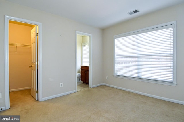 unfurnished bedroom with connected bathroom, a closet, light colored carpet, and a walk in closet