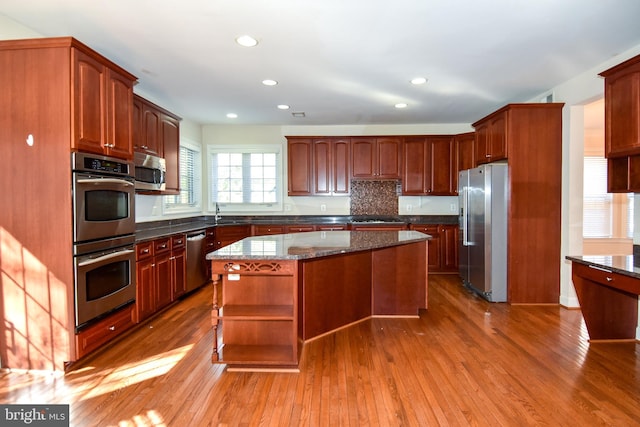 kitchen featuring a kitchen island, backsplash, hardwood / wood-style floors, stainless steel appliances, and dark stone countertops