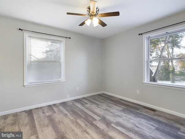 empty room with ceiling fan, a healthy amount of sunlight, and wood-type flooring