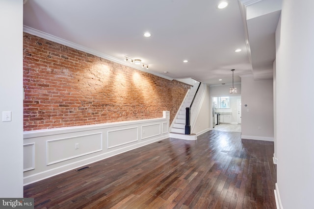 unfurnished living room featuring brick wall, crown molding, and dark hardwood / wood-style flooring