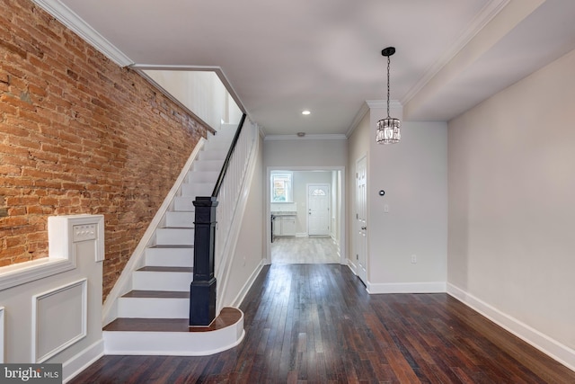 foyer entrance featuring ornamental molding, a chandelier, brick wall, and dark hardwood / wood-style flooring