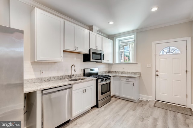 kitchen featuring sink, light wood-type flooring, white cabinetry, stainless steel appliances, and ornamental molding