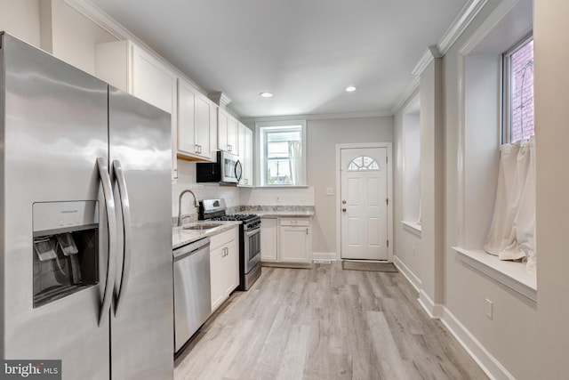 kitchen with light hardwood / wood-style flooring, sink, crown molding, white cabinets, and appliances with stainless steel finishes