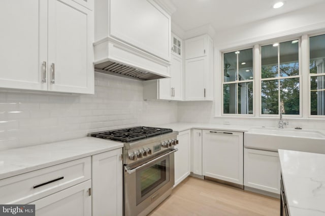 kitchen featuring high end range, light hardwood / wood-style floors, white cabinets, light stone counters, and premium range hood